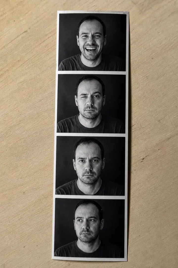 A black and white photo booth strip of four frames of the same man, lying on a wooden table.