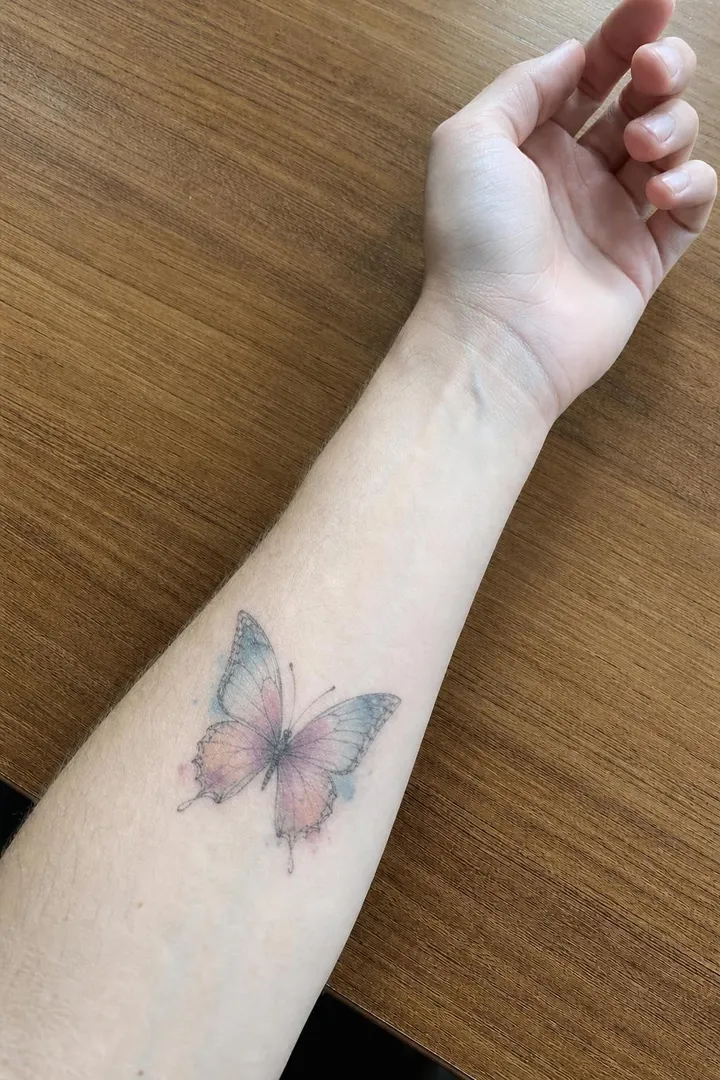 A watercolour butterfly with soft pink washes on the same forearm.